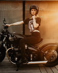 Woman sitting on a Motorcycle wearing a T-shirt with a women wearing a Motorcyclehelmet print and with the text "Wild dust sisters woman rider" and "Speed Goddess"