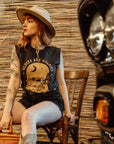 a young woman with a hat siting on a chair and wearing off-black tank top with brown motorcycle motive and oldies but goldies text