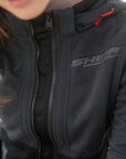 Person wearing a black jacket with 'SHINE' branding on a blurred background