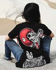 A woman siting on the beach wearing black Pando Moto women's motorcycle t-shirt with red scull motive