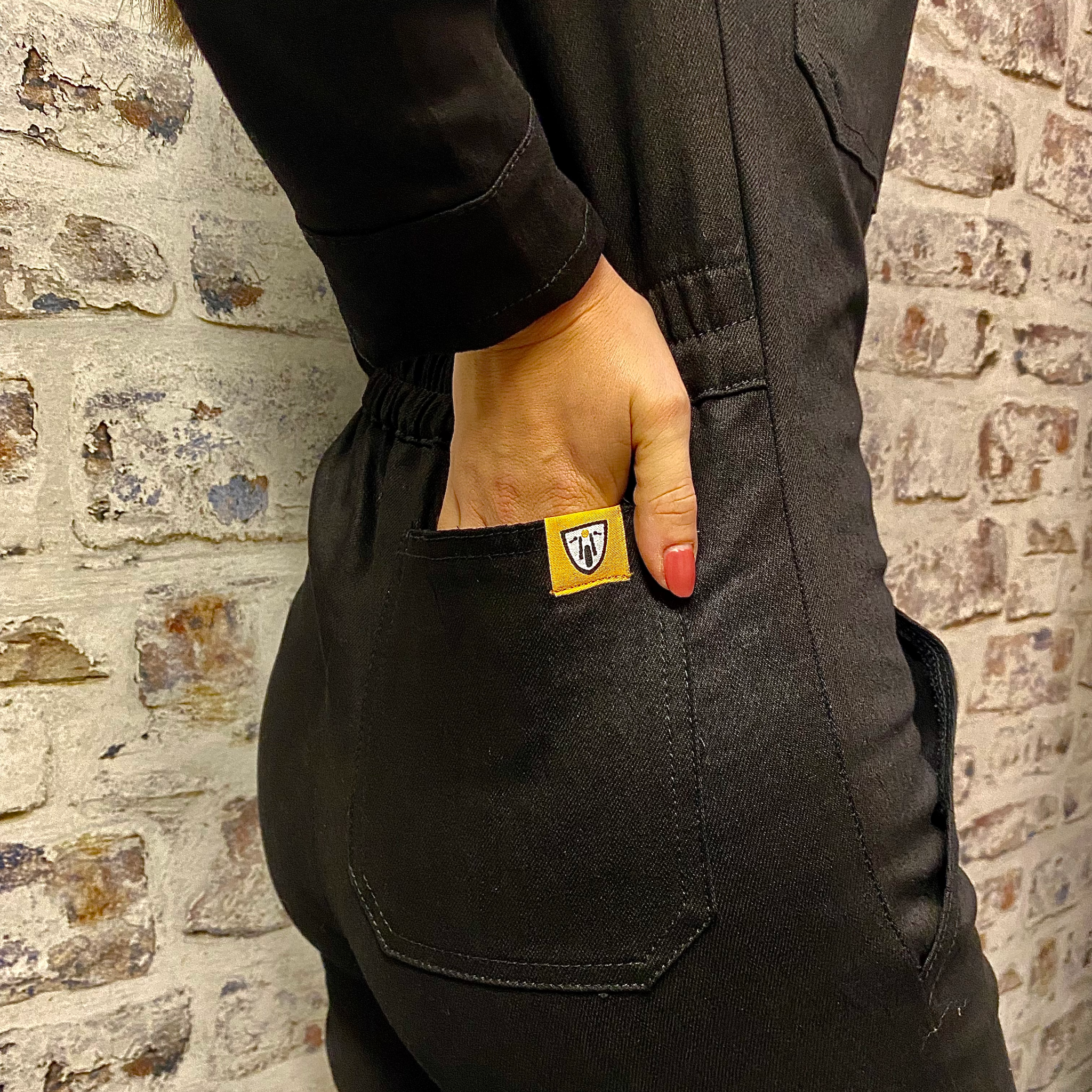 A close up of a woman holding her hand in the back pocket of black women's garage jumpsuit from MotoGirl