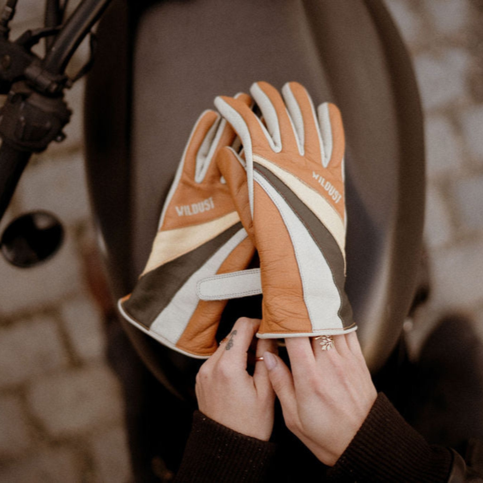 women's hands over a motorcycle gas tank while putting  on colourful leather gloves from WILDUST