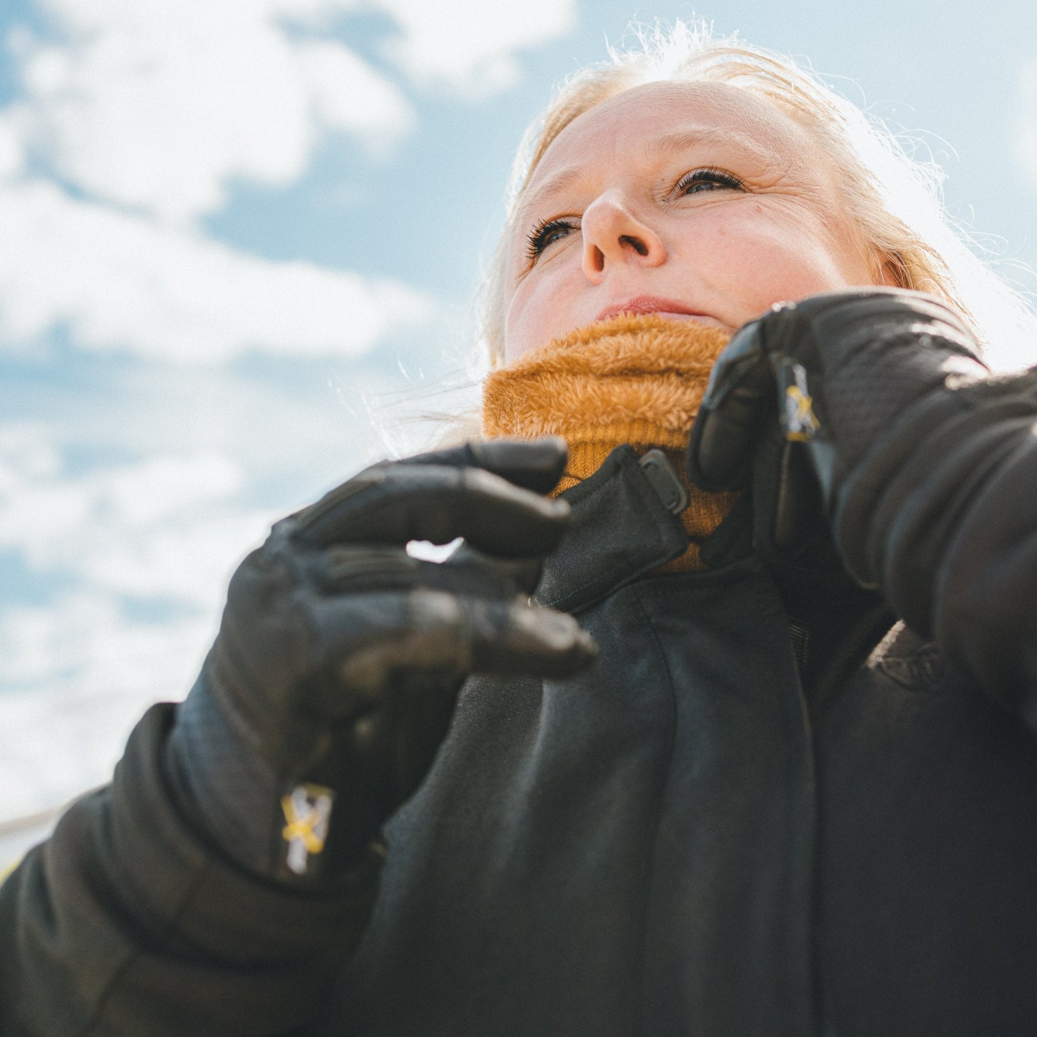 blond woman standing outside while wearing a caramel color knitted neck warmer from Moto Girl. 