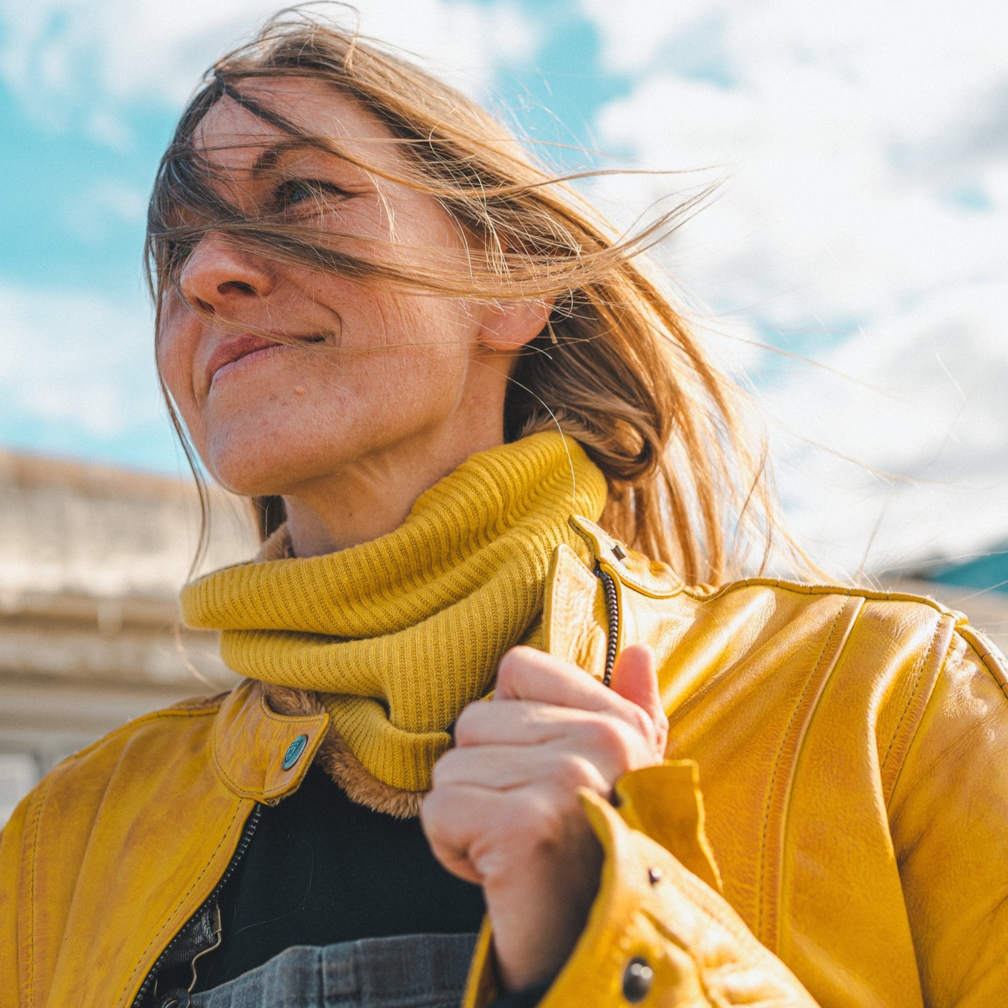 Woman standing outside wearing a yellow Valerie jacket and a yellow knitted neck warmer from Moto Girl.