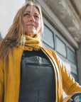 Woman standing outside against a wall, wearing a yellow Valerie jacket and a yellow knitted neck warmer from Moto Girl.