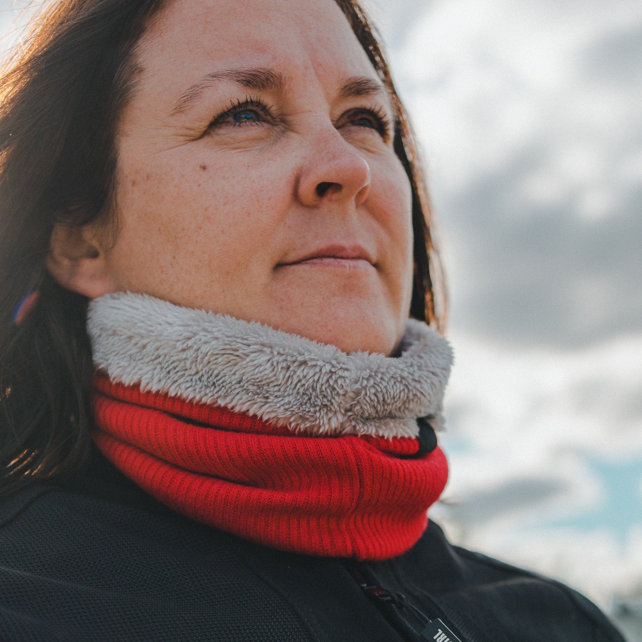 Woman standing outside wearing a black motorcycle jacket and a red knitted neck warmer from Moto Girl.