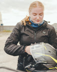 light red-haired woman wearing a blue knitted neck warmer from Moto Girl, standing with a helmet in her hands.