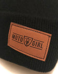 Close-up of the brown faux leather tag on the black beanie from MotoGirl, featuring the MotoGirl logo.