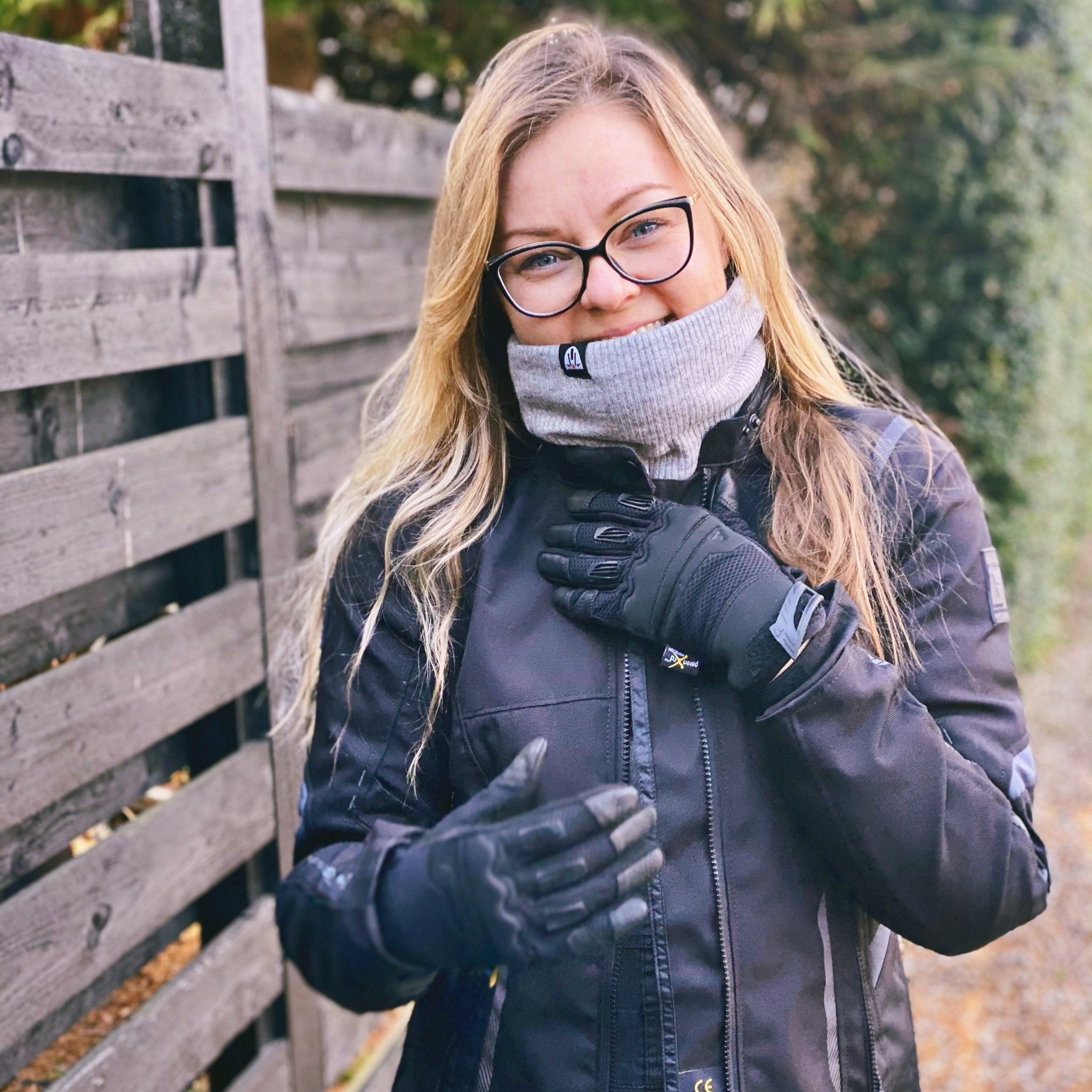 light haired woman in motorcycle gear wearing a light gray neck warmer from Moto Girl outside in nature