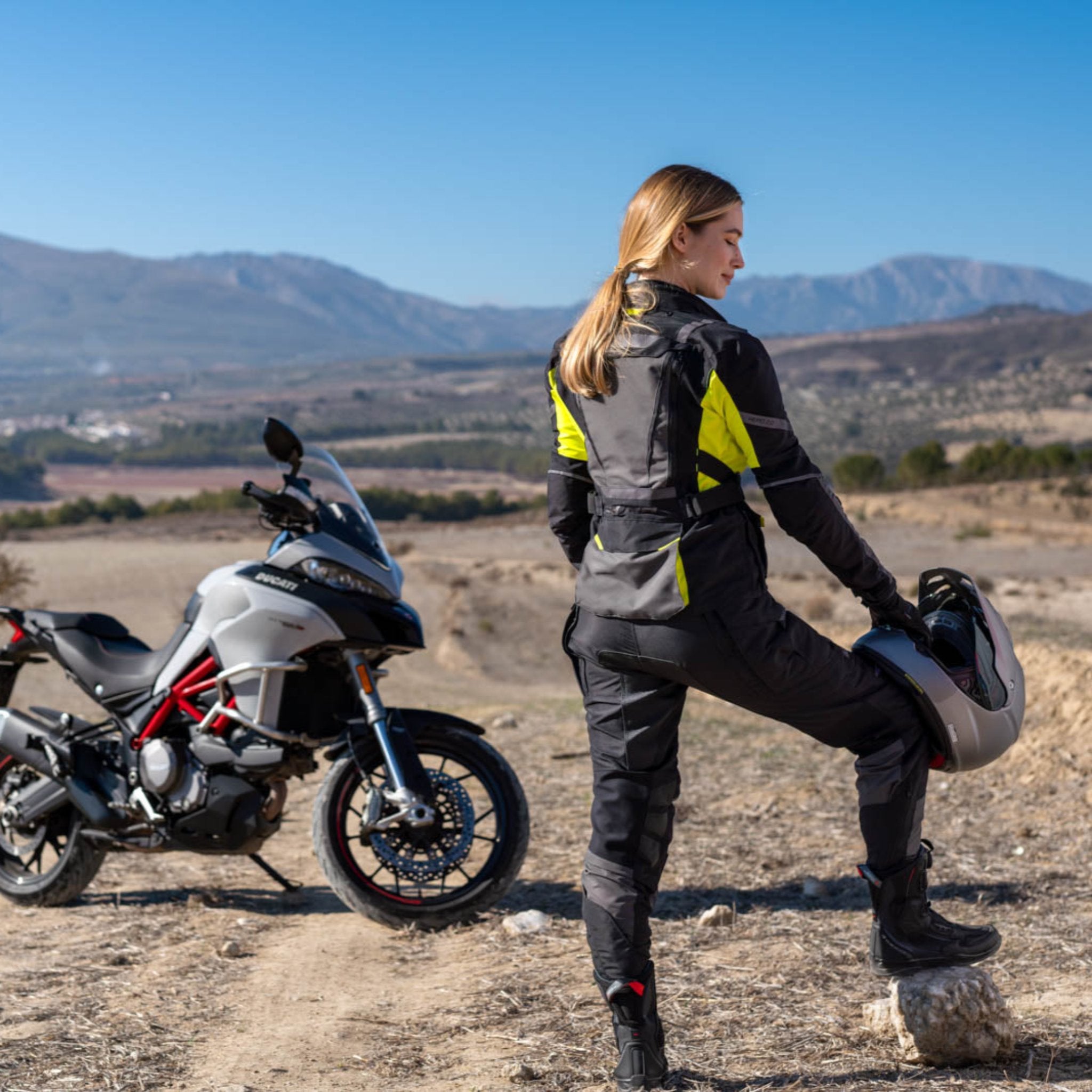 A woman standing by her motorcycle wearing Black SHIMA touring motorcycle pants for women