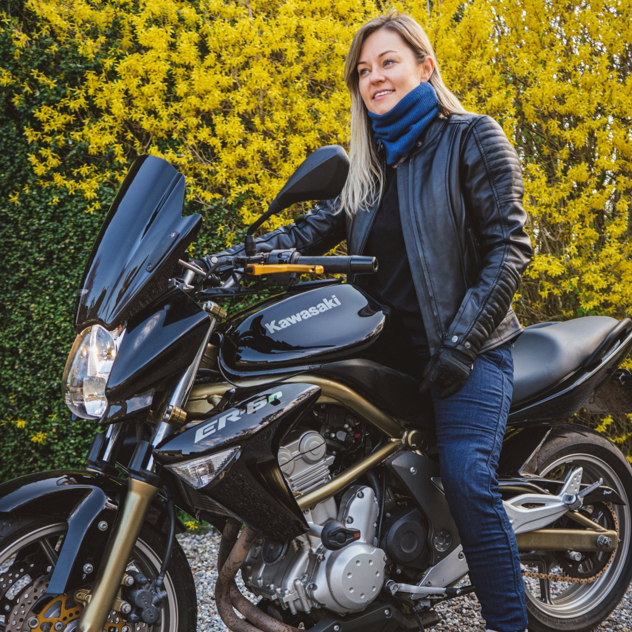 A blond woman on a motorcycle wearing black leather jacket 