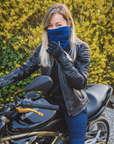 young light haired woman sitting on a Kawasaki motorcycle while wearing blue knitted neck warmer from Moto Girl and black Valerie jacket.