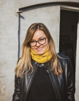 Smiling woman standing outside, wearing a black Valerie jacket and a yellow knitted neck warmer from Moto Girl.