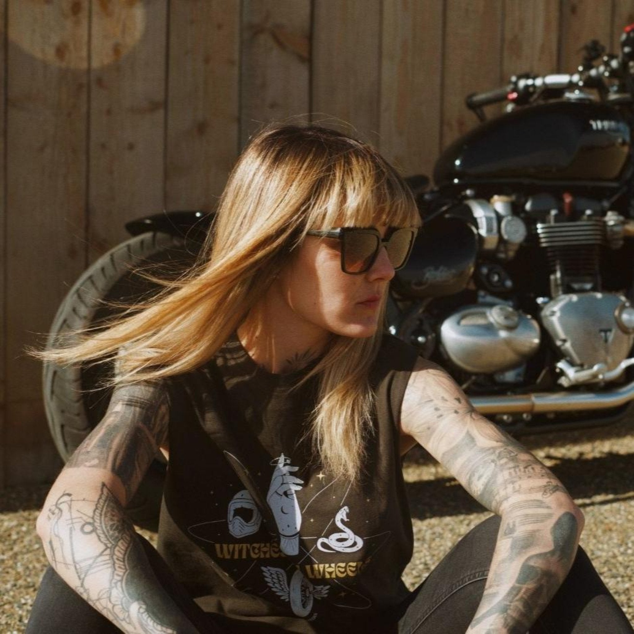 young woman siting by her motorcycle wearing witches of wheels t-shirt