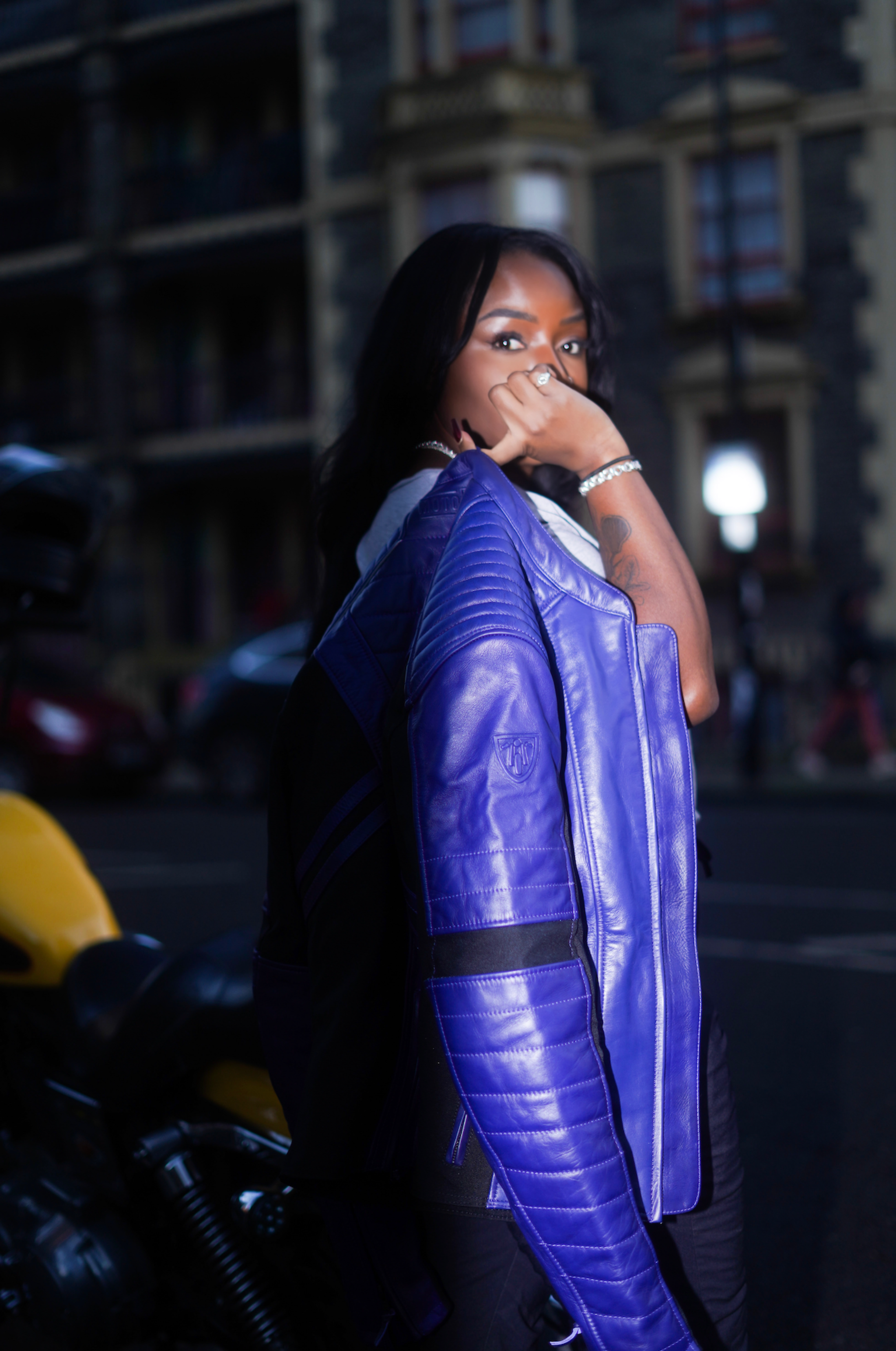 a black woman holding her purple motorcycle leather jacket on the shoulder