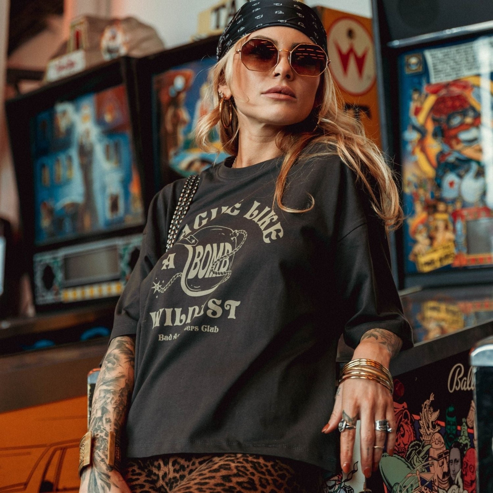 a young woman by game machines wearing off-black wide cut short sleeve women&#39;s motorcycle t-shirt with helmet motive and Fragile like a bomb  logo 