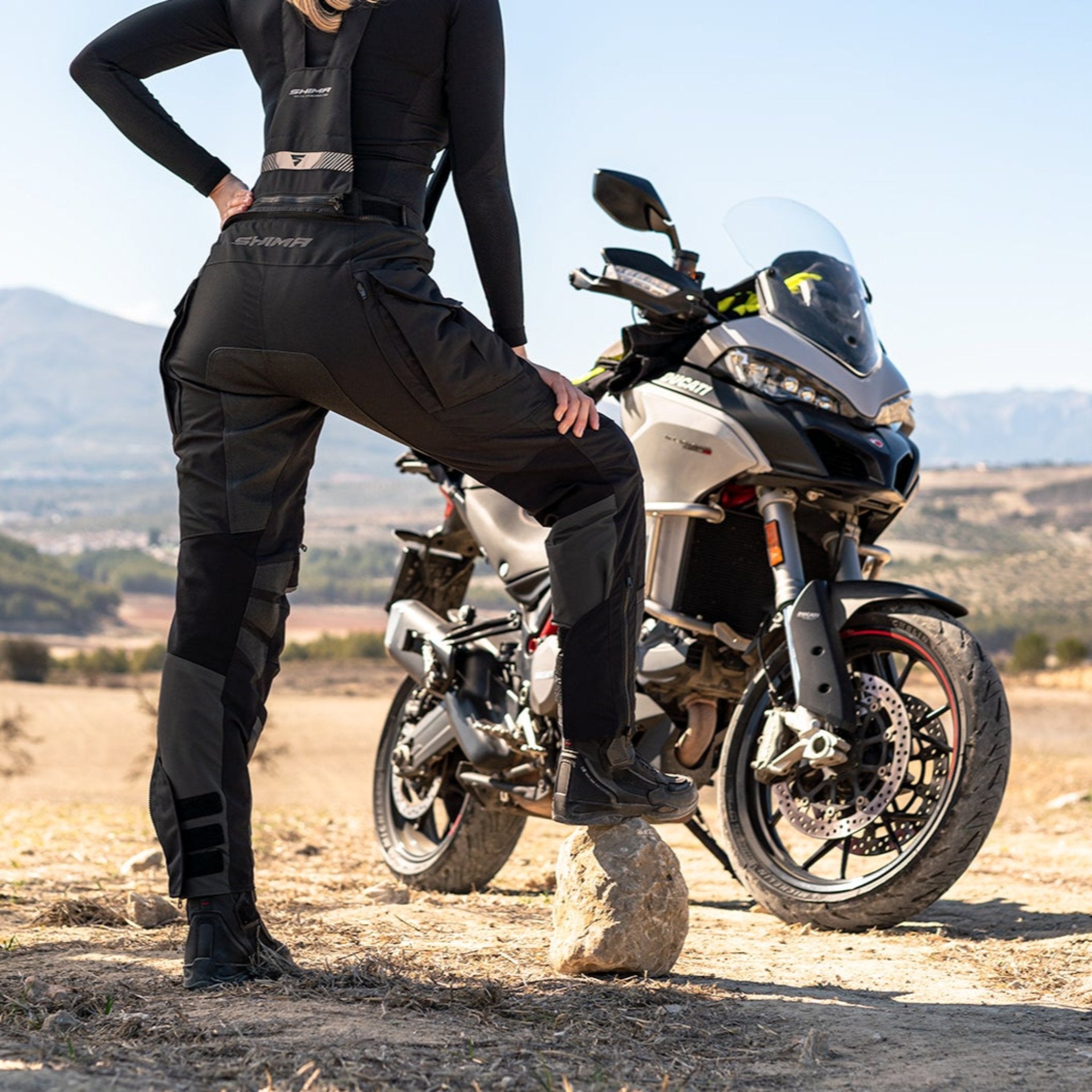 A woman standing by her motorcycle wearing Black SHIMA touring motorcycle pants for women 