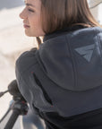 Person wearing a dark gray hoodie with a logo on a blurred background