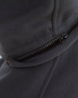 Close-up of a dark gray zippered hooded jacket or hoodie showing the zipper detail and part of a light gray geometric logo on the shoulder.
