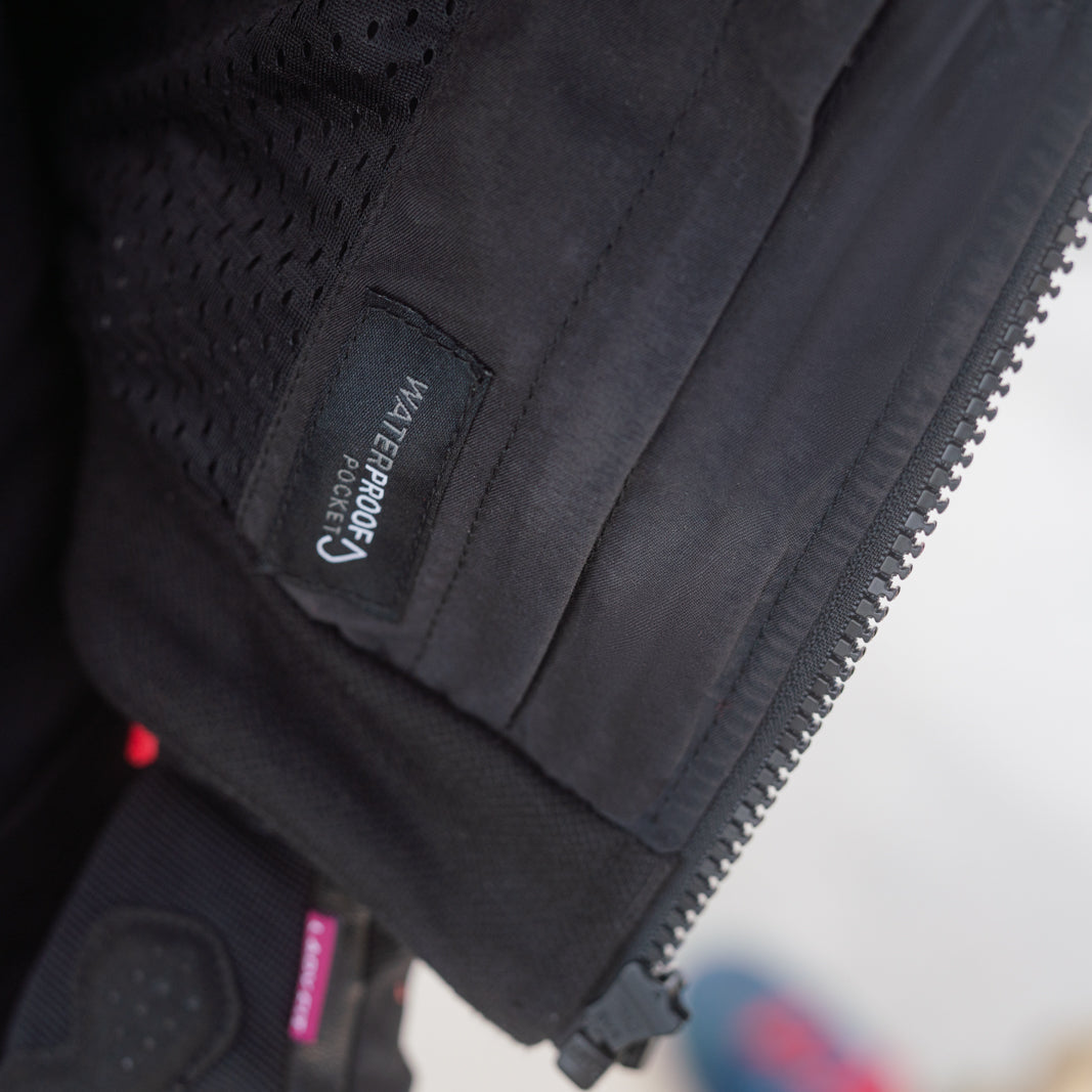 Close-up of a black technical jacket or vest showing the inner mesh lining, a zipper, and a small sewn label with white text.