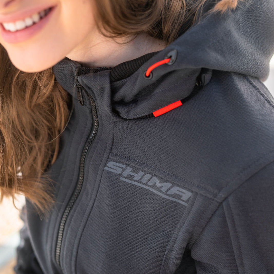 Person wearing a gray hoodie with 'Shima' branding, smiling outdoors.