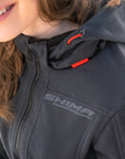 Person wearing a gray hoodie with 'Shima' branding, smiling outdoors.
