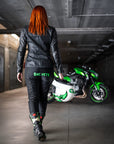 A red hair woman walking towards her motorcycle wearing black and red women's motorcycle leggings from exagon66