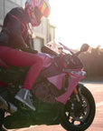 A woman wearing pink motorcycle trousers sitting on pink motorcycle