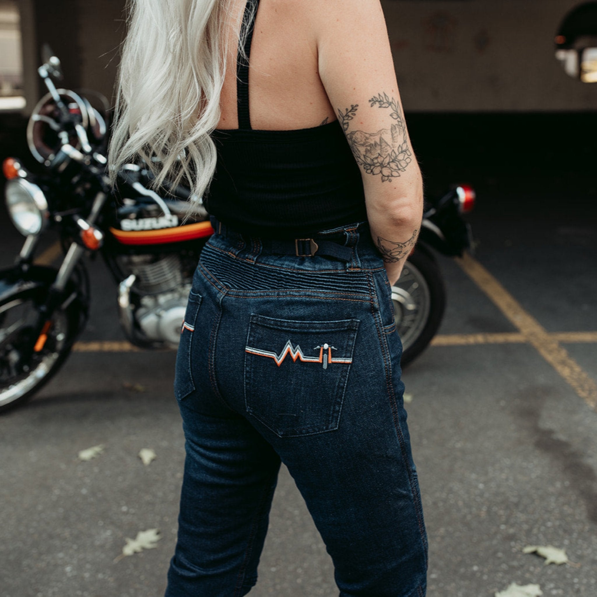 A tattooed woman on her Suzuki motorcycle wearing blue lady motorcycle jeans from Moto Girl.