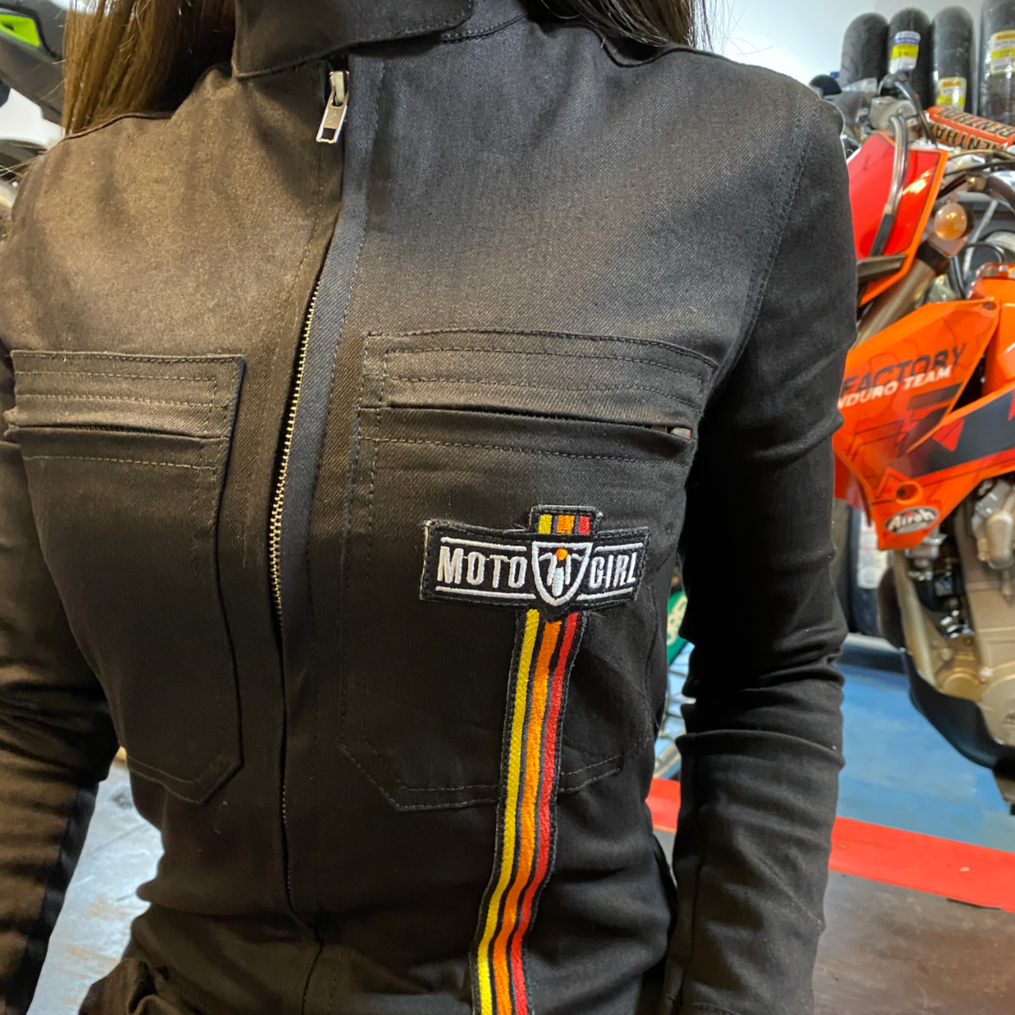 A close up of a woman&#39;s chest wearing black women&#39;s garage jumsuit with MotoGirl logo and stripe details