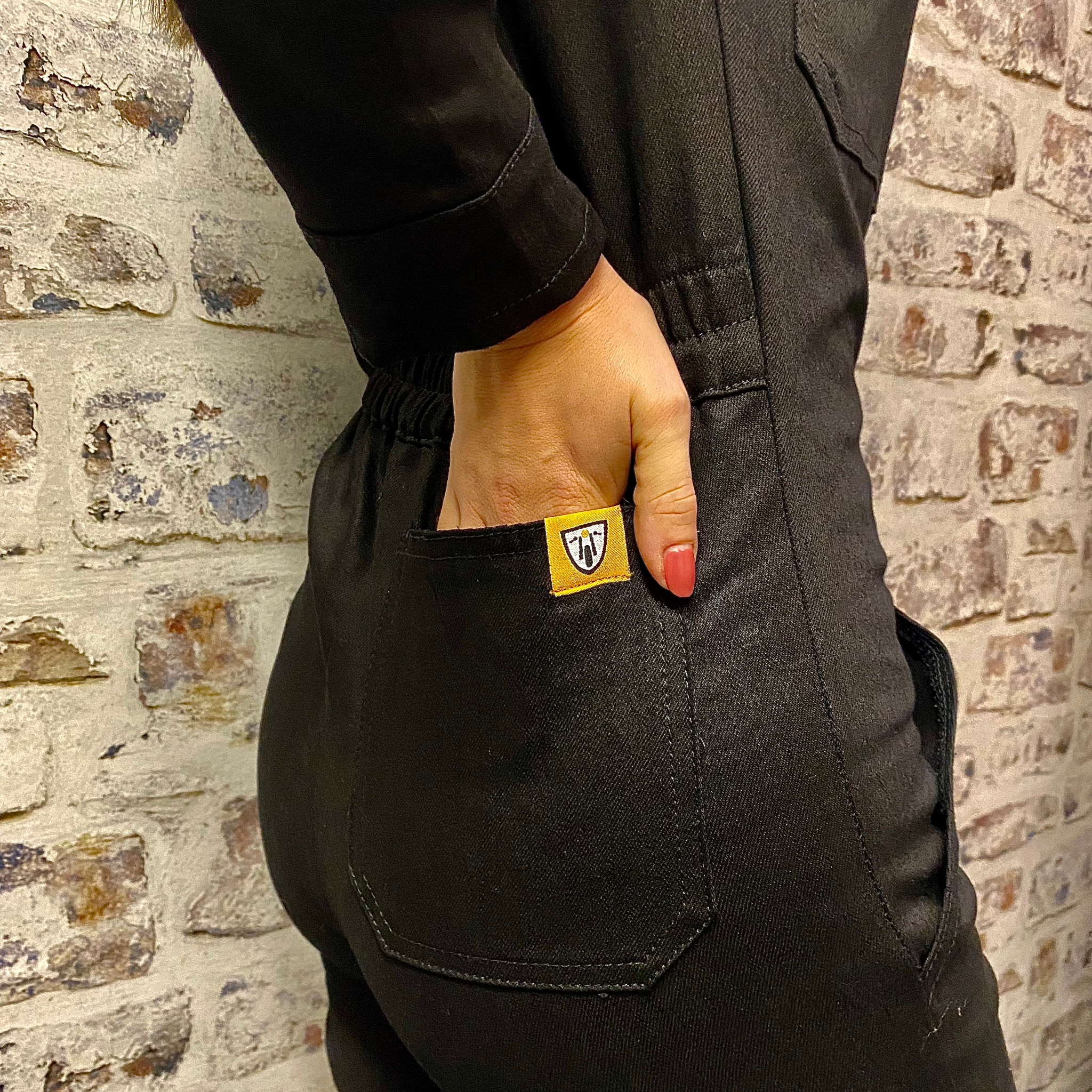 A close up of a woman holding her hand in the back pocket of black women&#39;s garage jumpsuit from MotoGirl