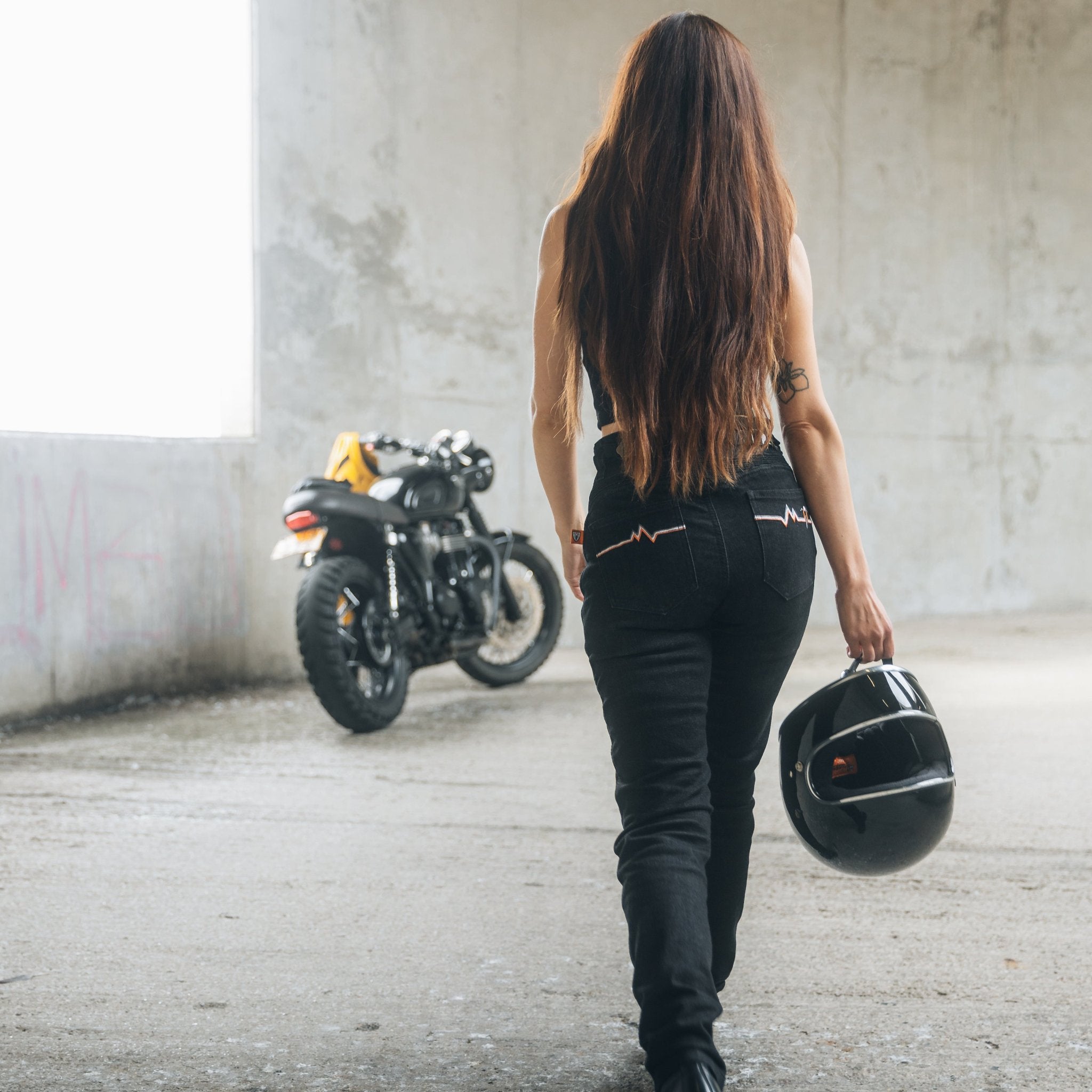 A woman walks towards her motorcycle wearing black women's motorcycle jeans from Moto Girl